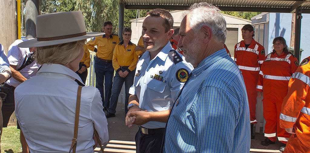 A two white men and one white women talking outdoors, with people in uniform in background