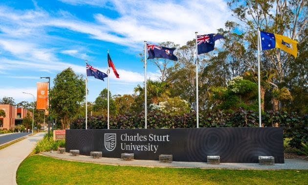 "Charles Sturt University" sign with multiple flags and trees in background