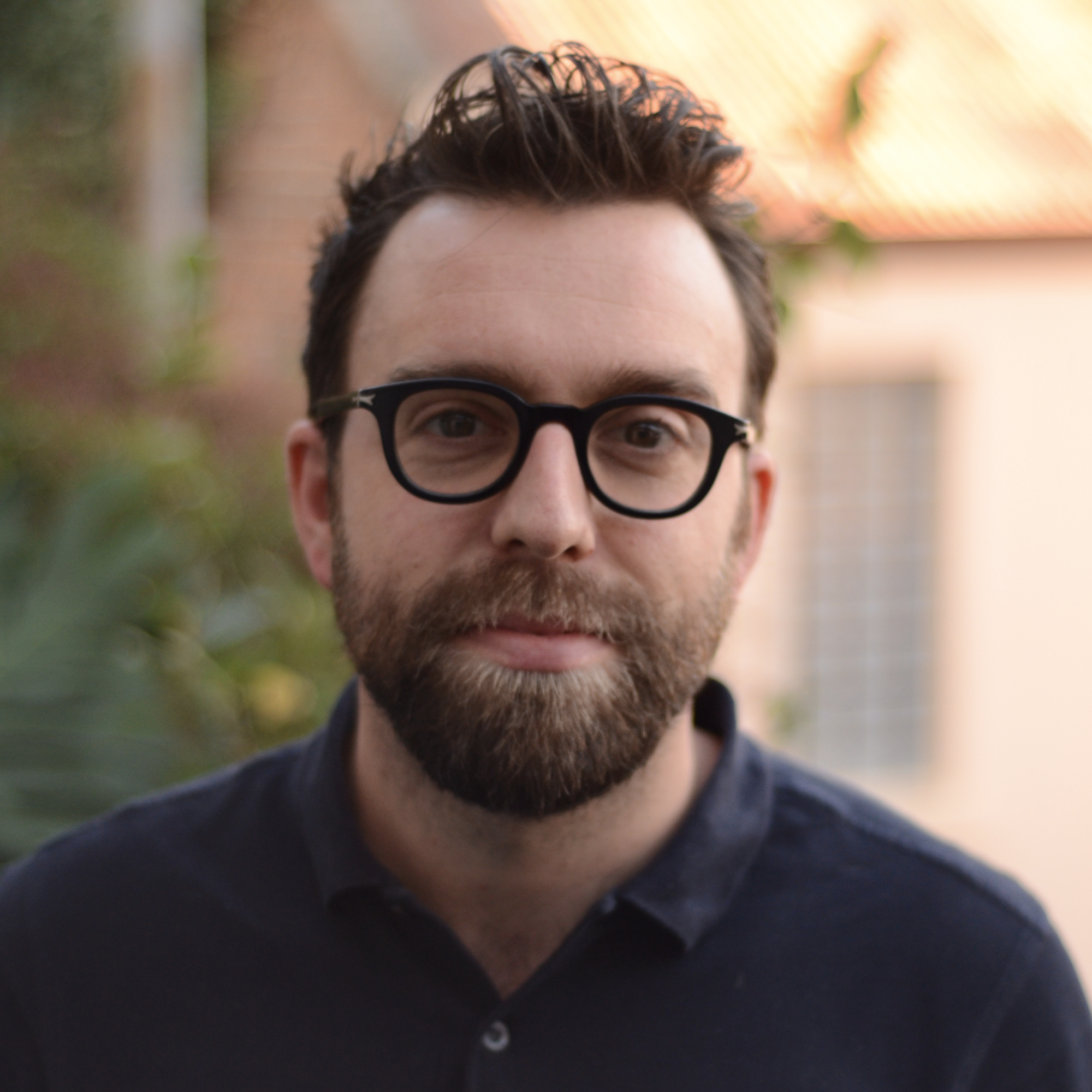 Headshot of white millennial man with glasses outdoors
