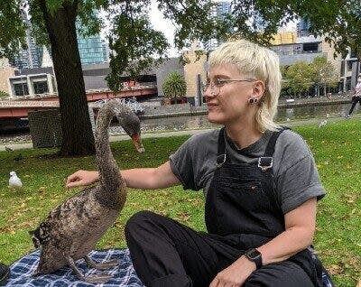 White women in overalls in a park petting a duck