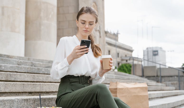 Woman checking message while holding hot beverage cup