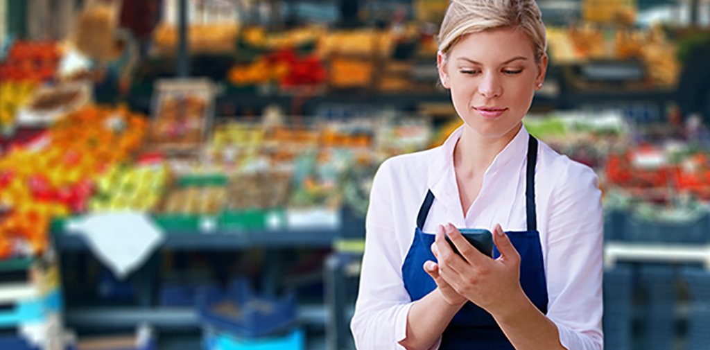 Young white woman wearing an apron in a grocery store, looking at a phone