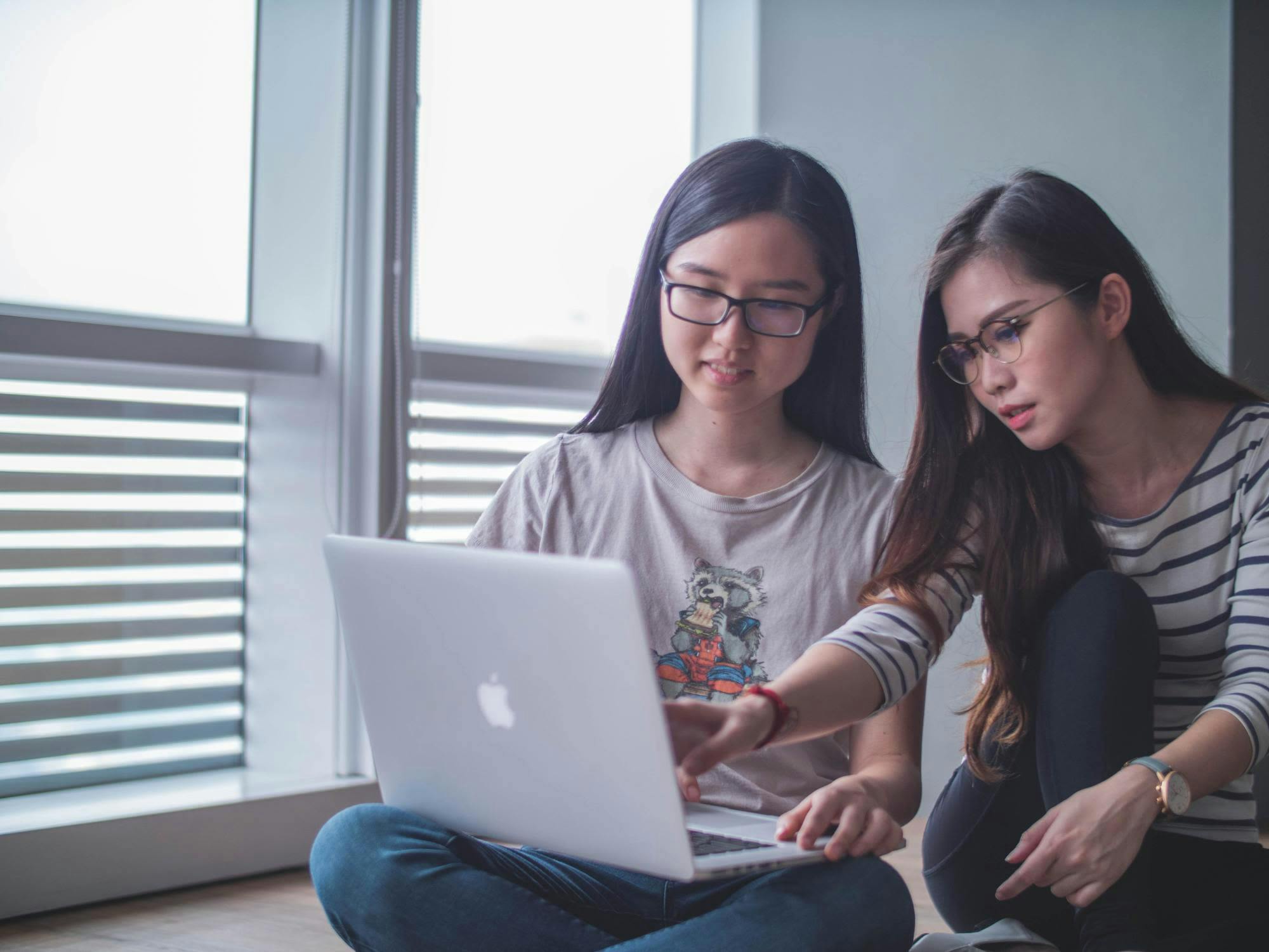 Two Asian girls in glasses looking at laptop