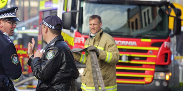 Fire fighter talking to two police officers in front of a firetruck