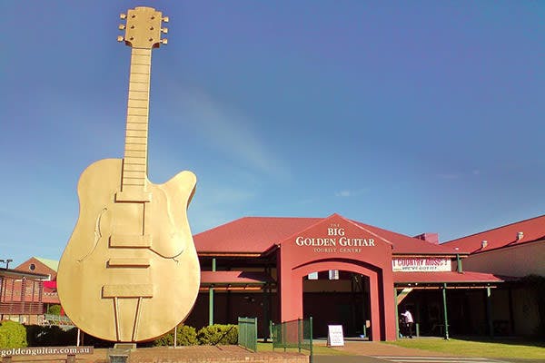 A huge golden guitar outside a building with signage "The Big Golden Guitar Tourist Centre"