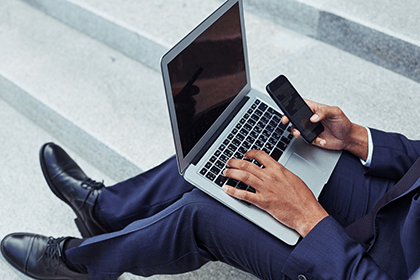 Lower half of black man in suit with cellphone and laptop