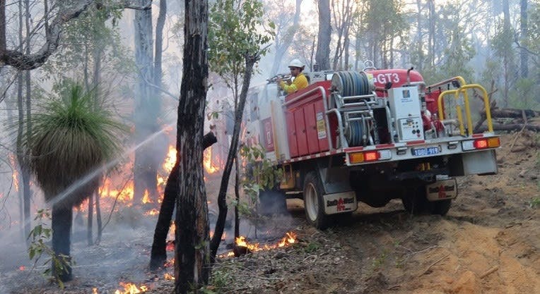 A firefighter on a fire truck using a hose on a bushfire