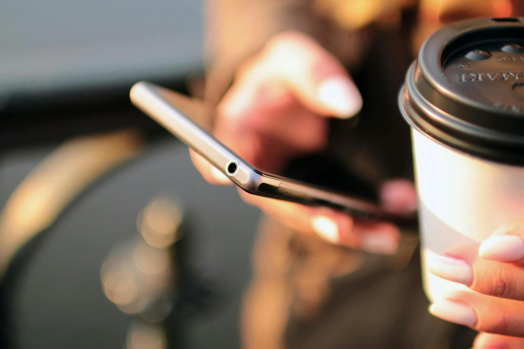 Close-up photo of a woman's hand holding a phone and coffee cup