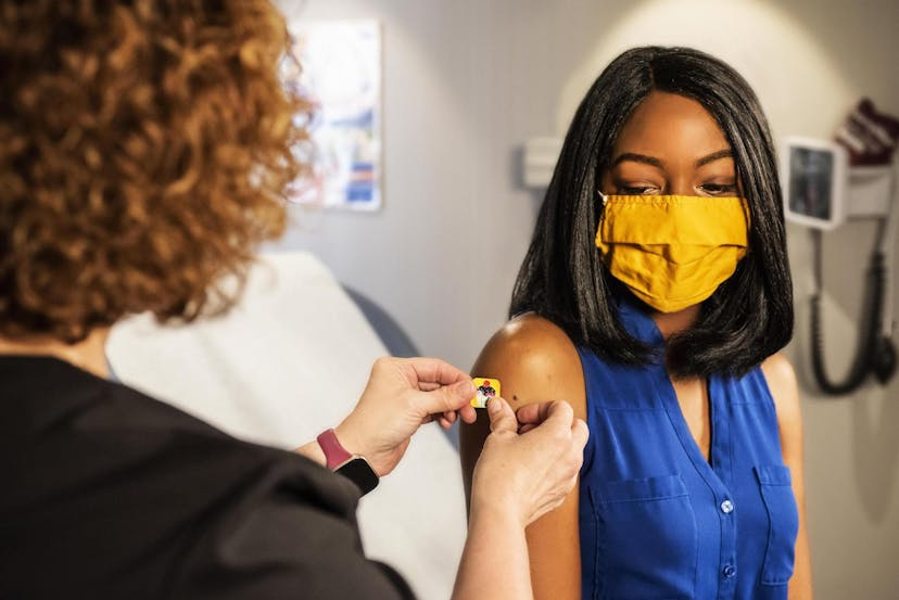 A healthcare worker applies a band-aid on a woman's arm after vaccination
