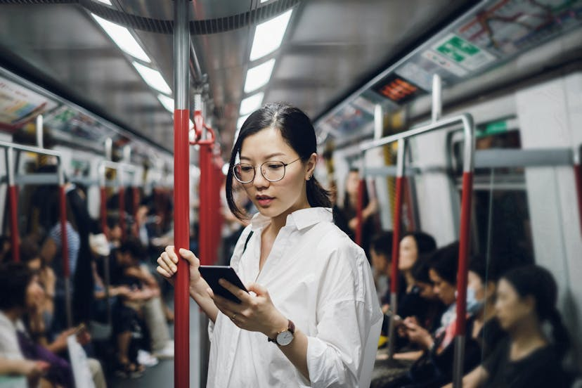 A woman stand in a train and using smartphone